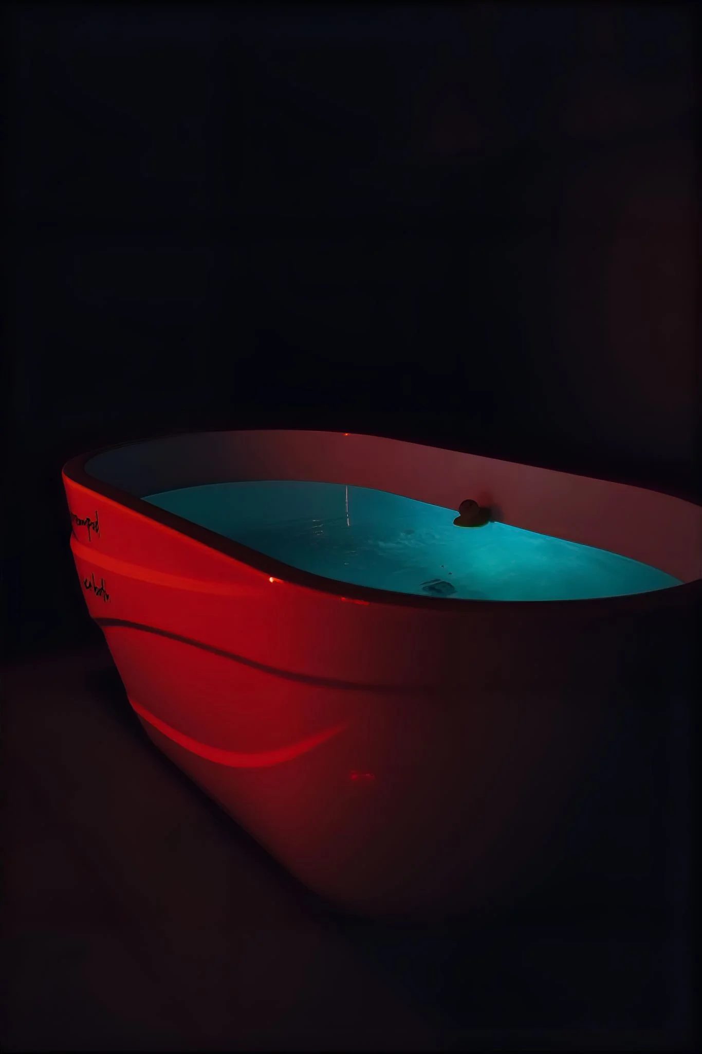 Red cold plunge tub filled with glowing teal 41-degree water in a dark room at Revive Wellness Place