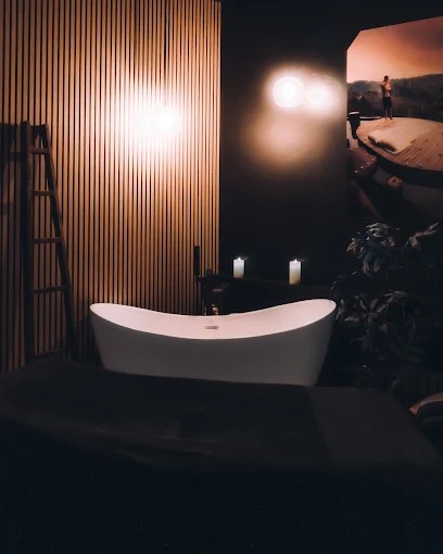 Dim, candlelit treatment room at Revive with a sculptural white soaking tub and warm wood slat wall
